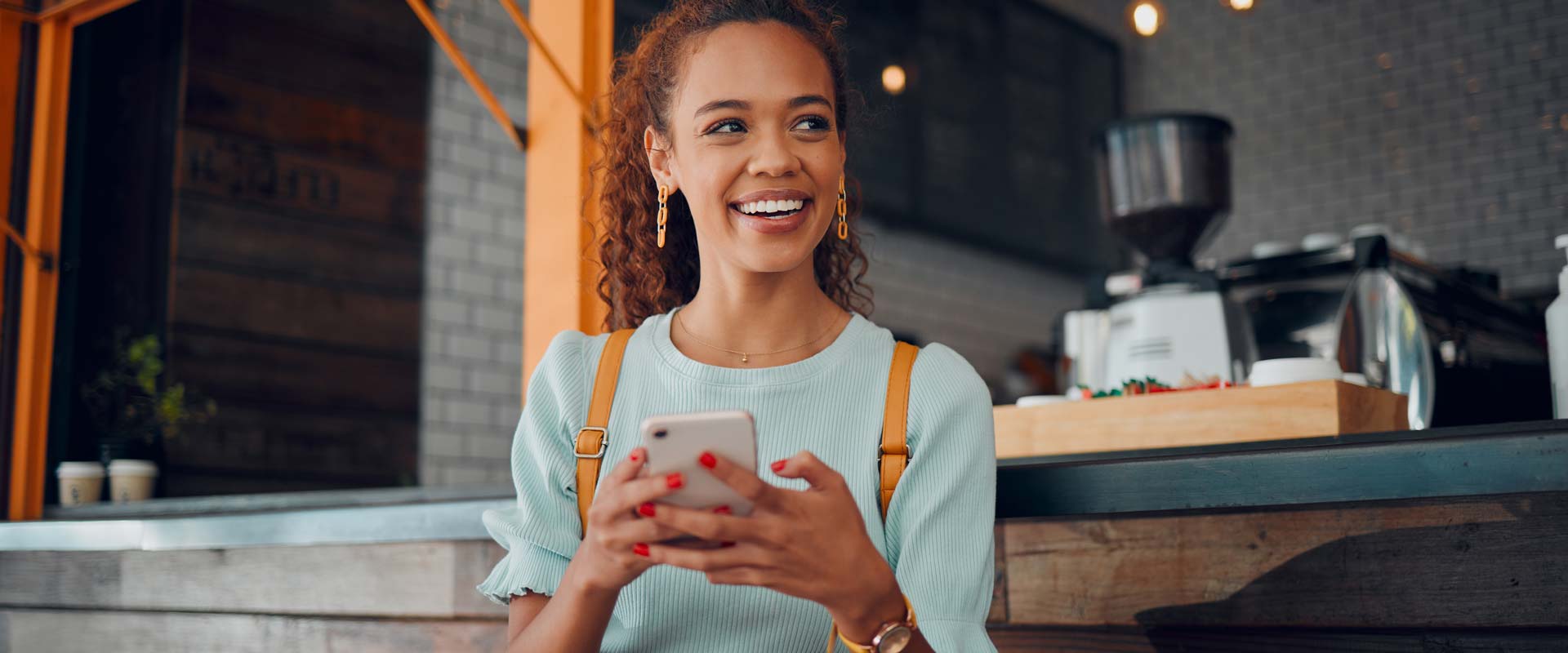 FollowMyMoney MyBroker Aktien, Fonds, ETFs, Optionsscheine traden - zufriedene junge Frau in einem Kaffee am Handy